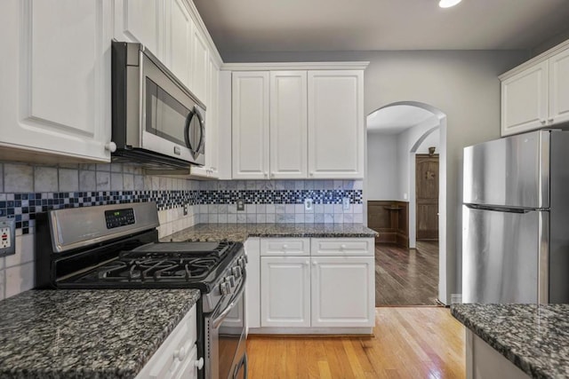 kitchen featuring light hardwood / wood-style flooring, appliances with stainless steel finishes, white cabinetry, decorative backsplash, and dark stone counters