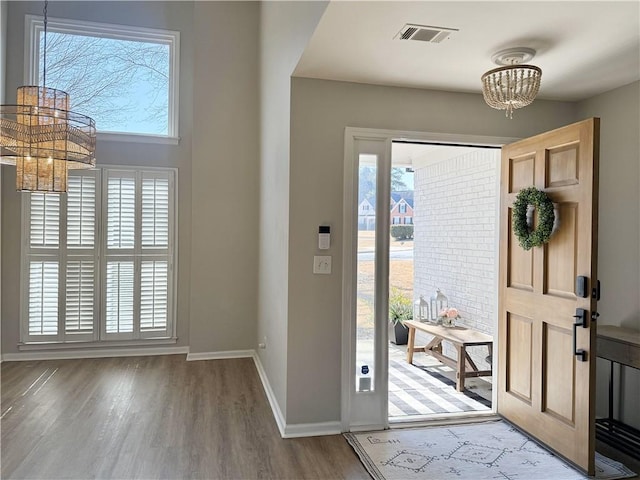 entrance foyer featuring baseboards, wood finished floors, visible vents, and a notable chandelier