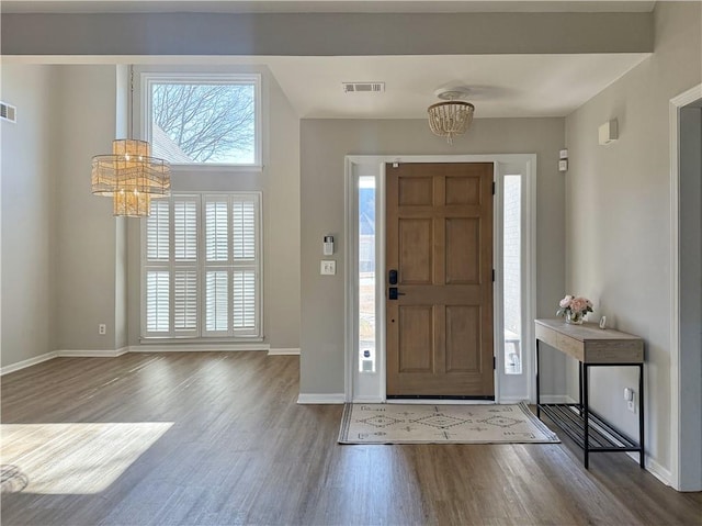 foyer entrance with a chandelier, visible vents, baseboards, and wood finished floors