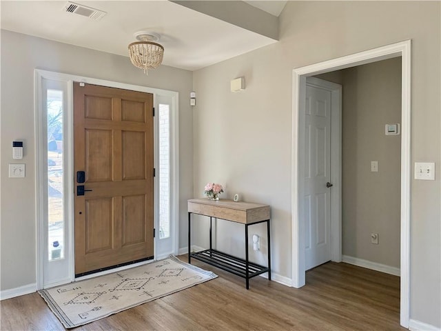 foyer entrance with a notable chandelier, baseboards, visible vents, and wood finished floors