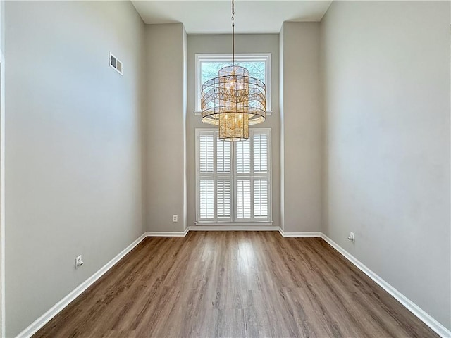 unfurnished dining area with an inviting chandelier, visible vents, baseboards, and wood finished floors