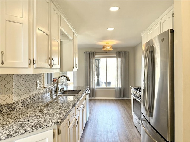 kitchen with stone counters, stainless steel appliances, decorative backsplash, white cabinetry, and a sink