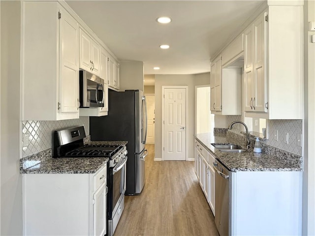 kitchen with stainless steel appliances, white cabinetry, light wood-style floors, and dark stone countertops