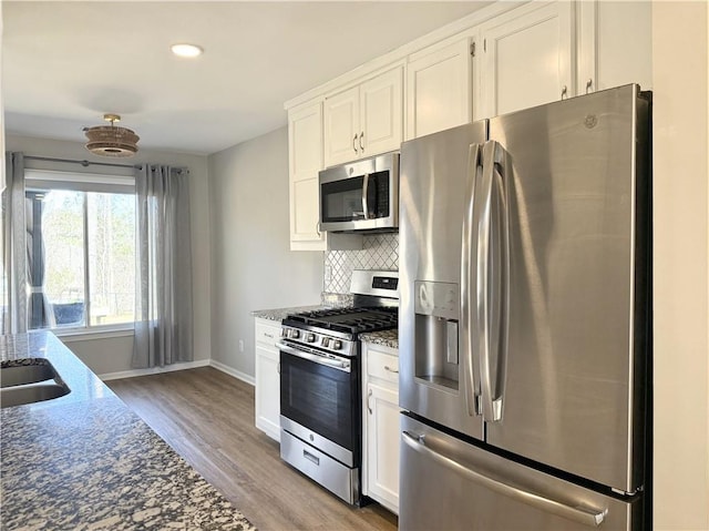 kitchen featuring stainless steel appliances, light wood-style floors, white cabinets, dark stone counters, and tasteful backsplash