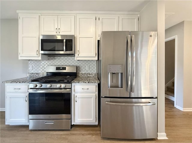 kitchen featuring tasteful backsplash, appliances with stainless steel finishes, white cabinets, and dark stone countertops