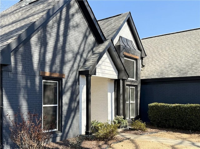 view of property exterior featuring a shingled roof and brick siding