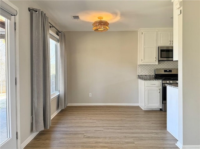 kitchen featuring stainless steel appliances, visible vents, white cabinetry, light wood-style floors, and tasteful backsplash