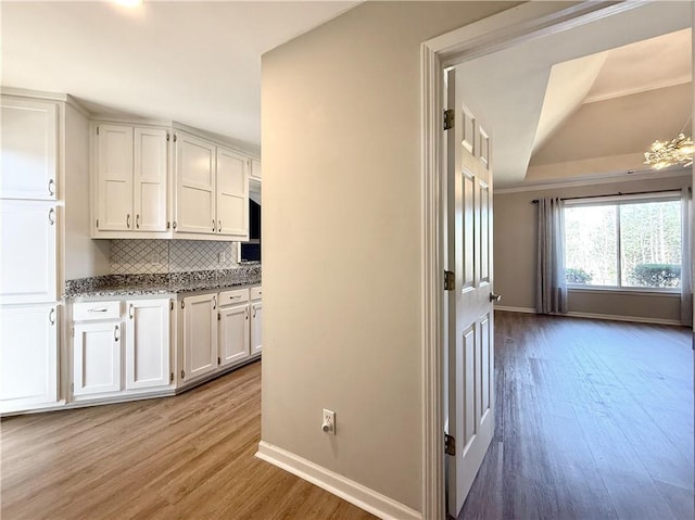 kitchen featuring light wood-type flooring, tasteful backsplash, baseboards, and white cabinets