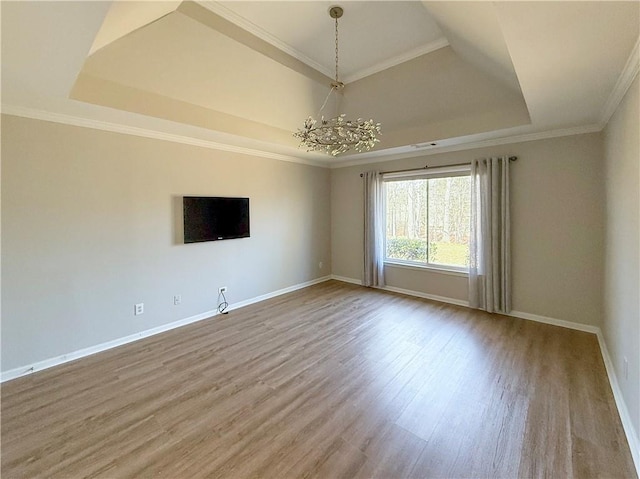 unfurnished living room featuring a chandelier, wood finished floors, baseboards, ornamental molding, and a tray ceiling