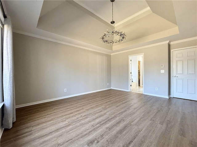 unfurnished room featuring baseboards, ornamental molding, wood finished floors, an inviting chandelier, and a tray ceiling