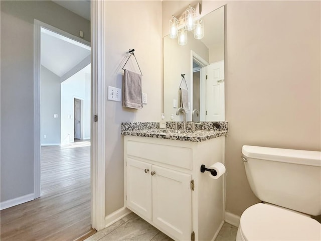 half bath with baseboards, vanity, toilet, and wood finished floors