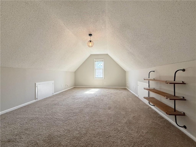 additional living space featuring a textured ceiling, baseboards, vaulted ceiling, and carpet flooring