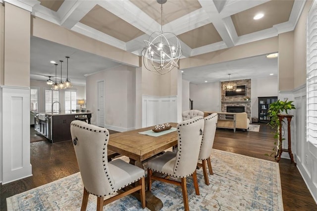 dining room with a notable chandelier, coffered ceiling, dark wood-type flooring, and a large fireplace