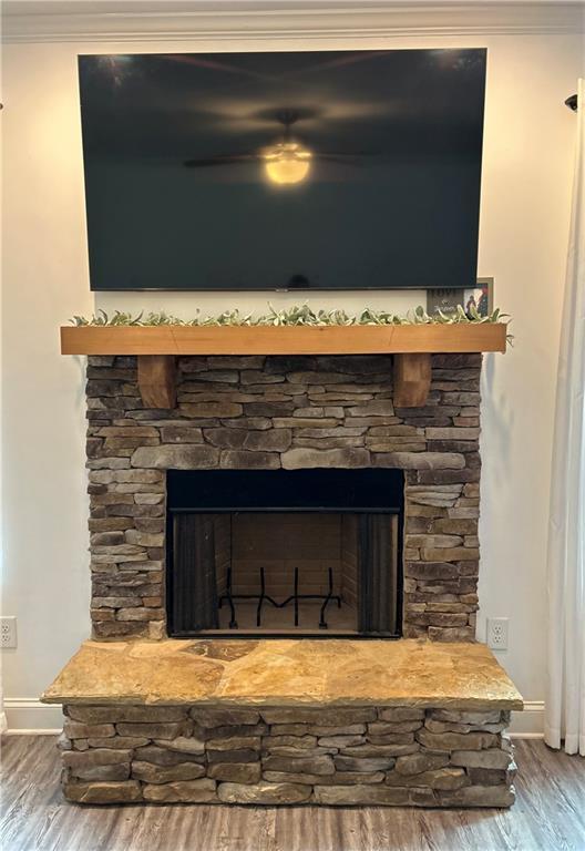 detailed view of a stone fireplace, ornamental molding, wood finished floors, and a ceiling fan