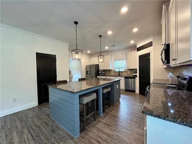 kitchen featuring appliances with stainless steel finishes, a breakfast bar, backsplash, dark wood-style flooring, and a center island