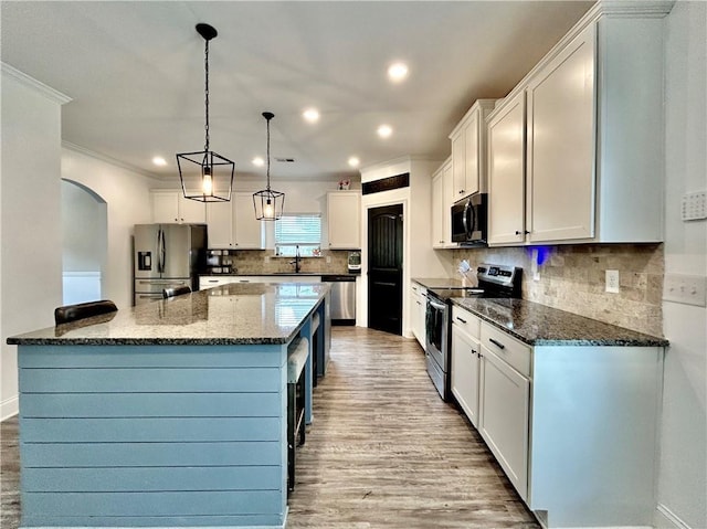 kitchen with stainless steel appliances, light wood-type flooring, crown molding, a sink, and dark stone countertops