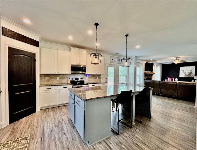 kitchen with appliances with stainless steel finishes, a center island, white cabinets, dark stone counters, and light wood-type flooring