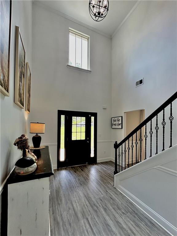 entryway with ornamental molding, stairway, a chandelier, wood finished floors, and baseboards