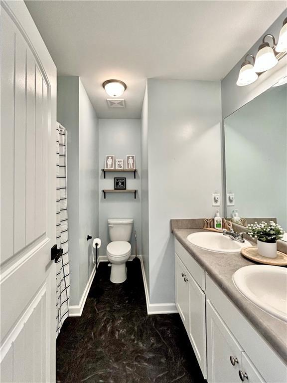 full bath with toilet, baseboards, and double vanity
