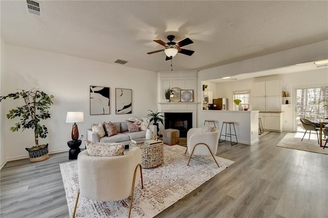 living room featuring light wood-style flooring, a fireplace, visible vents, and a ceiling fan