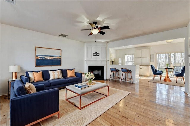 living room with visible vents, a fireplace, light wood finished floors, and ceiling fan