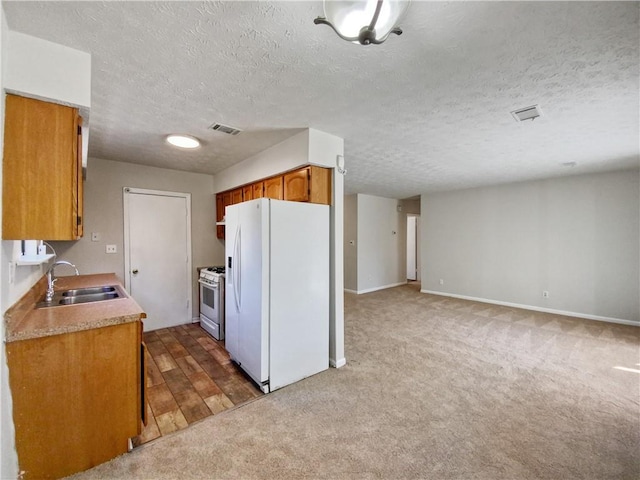 kitchen featuring a textured ceiling, dark carpet, white appliances, and sink