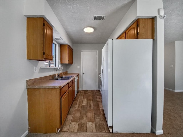 kitchen with a textured ceiling, light wood-type flooring, white appliances, and sink