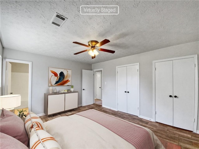 bedroom with hardwood / wood-style flooring, ceiling fan, a textured ceiling, and two closets