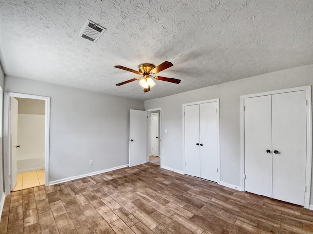 unfurnished bedroom featuring wood-type flooring, connected bathroom, ceiling fan, and multiple closets