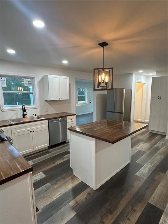 kitchen with stainless steel appliances, pendant lighting, white cabinets, a kitchen island, and butcher block counters