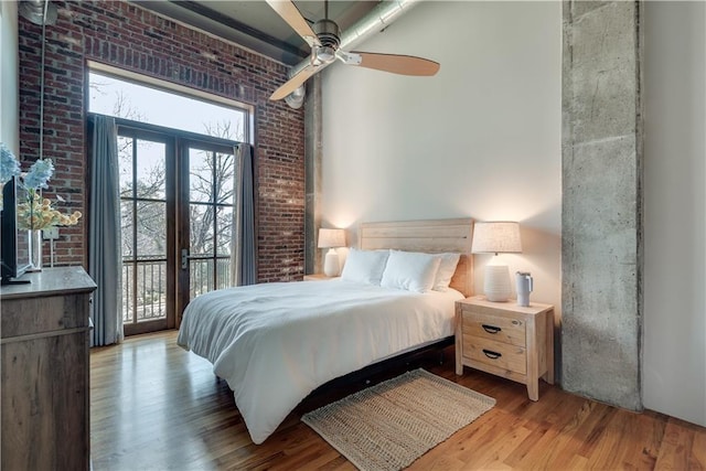 bedroom with access to outside, light wood-type flooring, ceiling fan, and brick wall