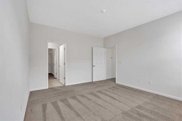 unfurnished bedroom featuring a walk in closet, light colored carpet, and a closet