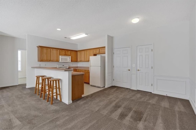 kitchen with a kitchen bar, a center island, light colored carpet, and white appliances