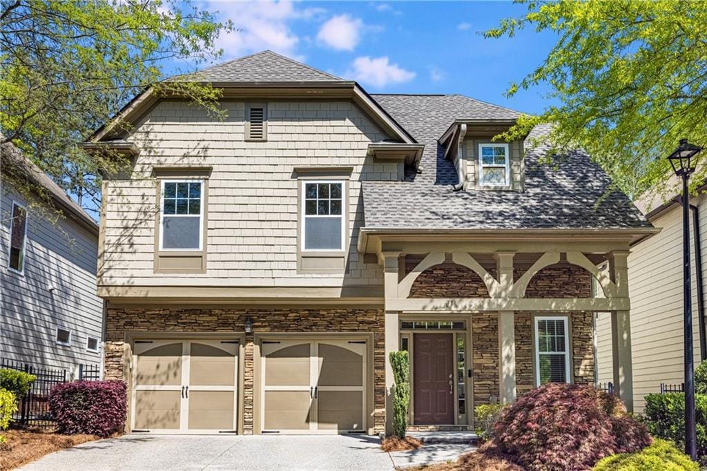 view of front of property featuring a shingled roof, stone siding, a garage, and concrete driveway