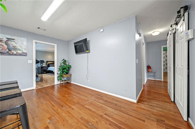 interior space with a barn door, baseboards, visible vents, wood finished floors, and a textured ceiling