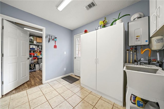 kitchen with light tile patterned floors, visible vents, tankless water heater, a textured ceiling, and a sink