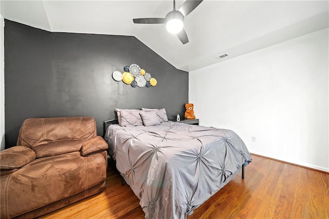 bedroom with an accent wall, wood finished floors, visible vents, a ceiling fan, and vaulted ceiling