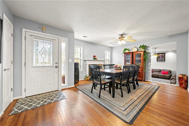 dining area featuring light wood-style flooring, a fireplace, baseboards, and a textured ceiling