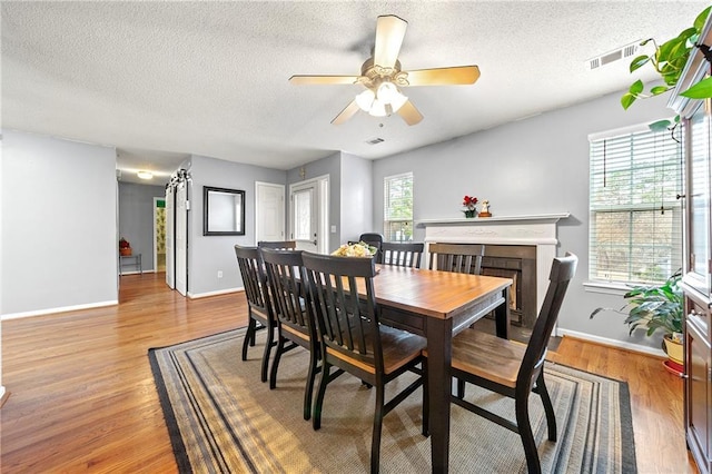 dining room with a fireplace, visible vents, light wood-style flooring, a textured ceiling, and baseboards