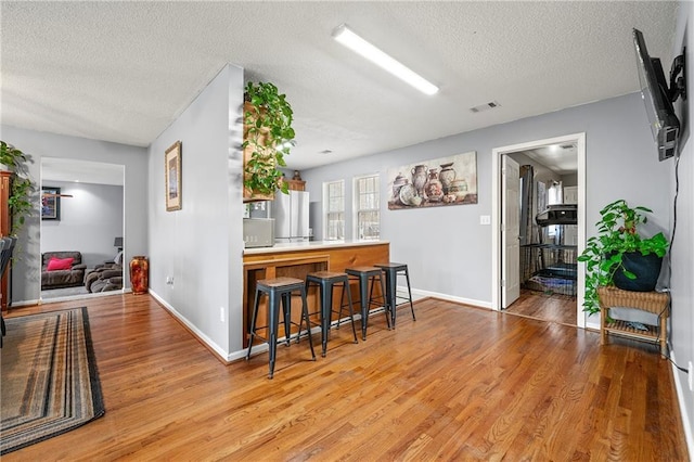 kitchen featuring visible vents, light wood-style flooring, a kitchen breakfast bar, freestanding refrigerator, and a textured ceiling