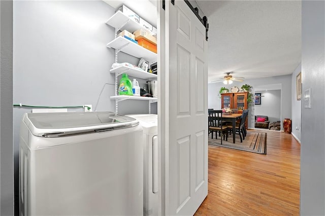 laundry room featuring ceiling fan, a barn door, light wood-style flooring, laundry area, and washing machine and clothes dryer