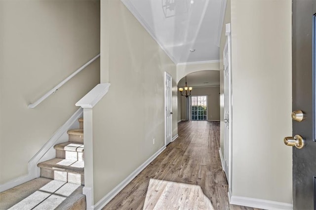 entrance foyer with stairway, wood finished floors, arched walkways, crown molding, and a notable chandelier