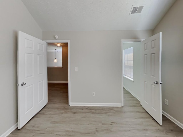 unfurnished bedroom featuring vaulted ceiling, baseboards, light wood-type flooring, and visible vents