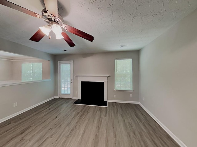 unfurnished living room with wood finished floors, a fireplace, visible vents, baseboards, and ceiling fan