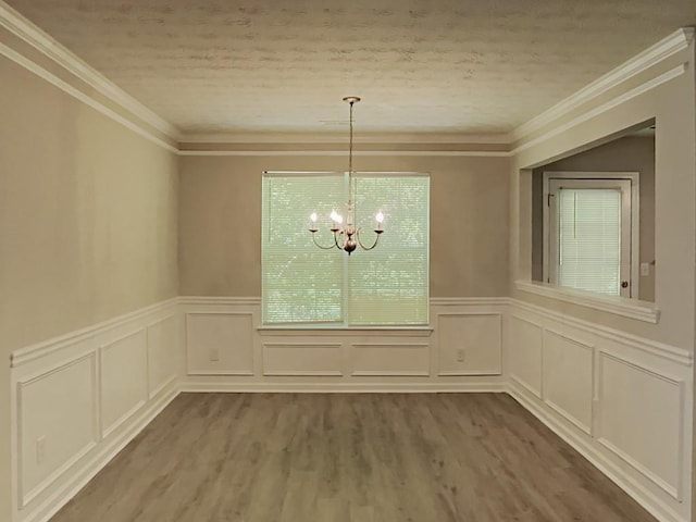 unfurnished dining area featuring a decorative wall, an inviting chandelier, a wainscoted wall, and wood finished floors