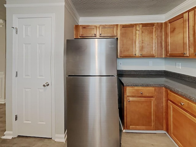 kitchen featuring freestanding refrigerator, brown cabinetry, ornamental molding, and dark stone countertops