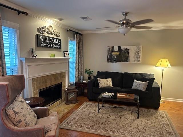 living room featuring a tiled fireplace, crown molding, ceiling fan, and wood-type flooring