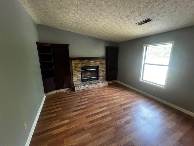 unfurnished living room featuring wood finished floors, baseboards, a fireplace, lofted ceiling, and a textured ceiling