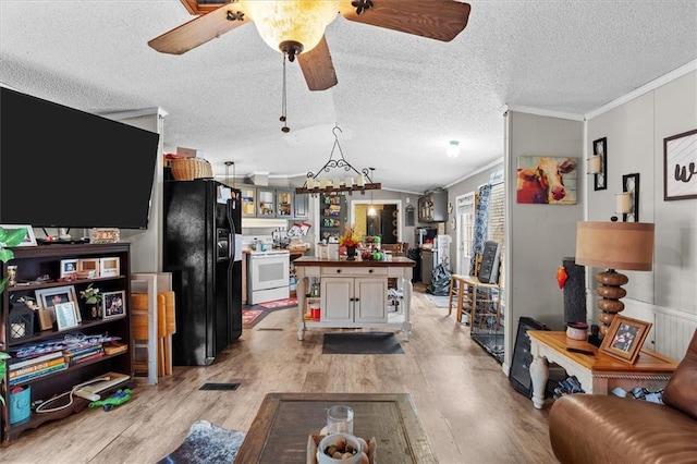 living area featuring a ceiling fan, a textured ceiling, crown molding, light wood finished floors, and lofted ceiling