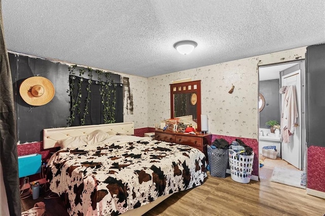 bedroom with wallpapered walls, wood finished floors, and a textured ceiling